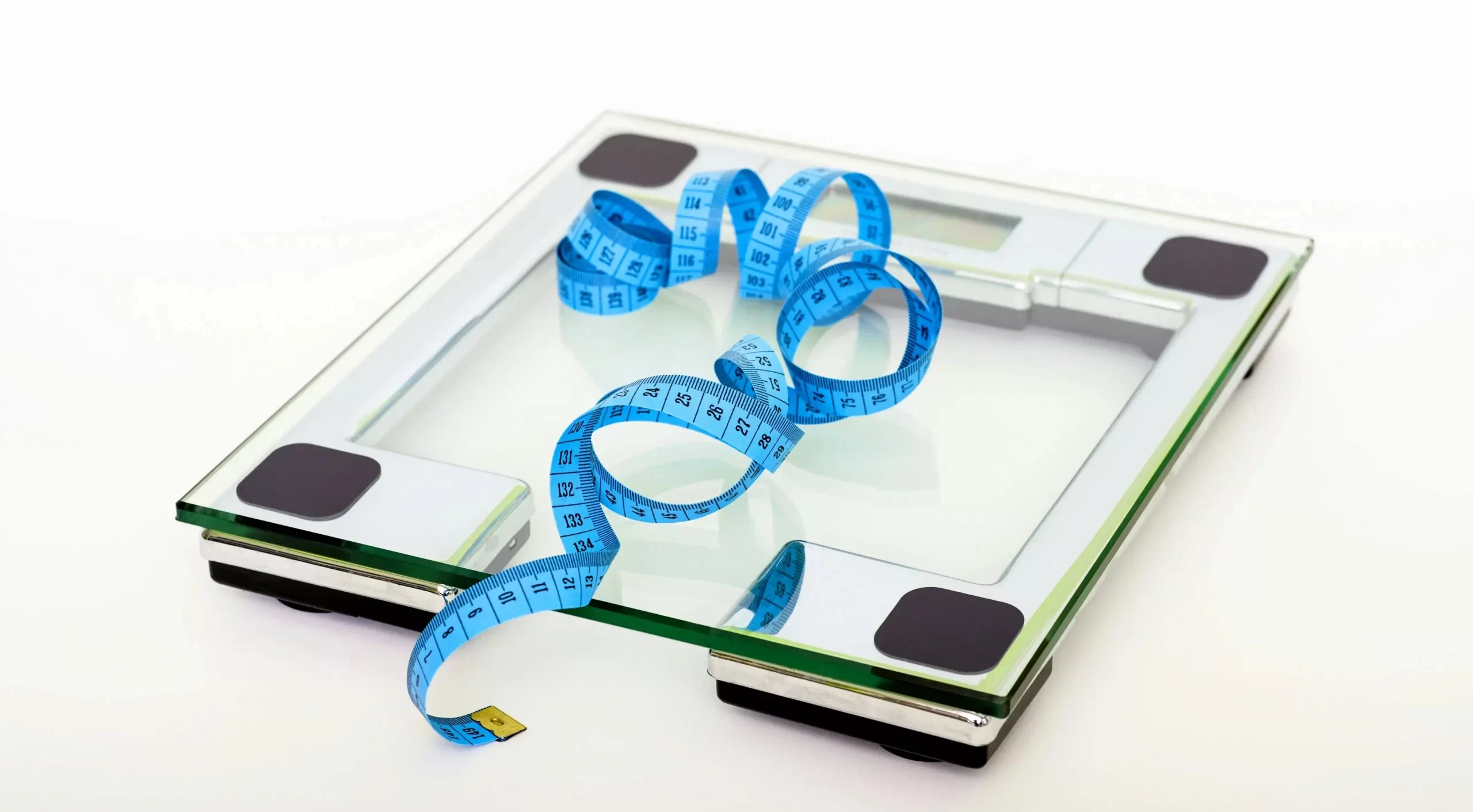 A weight scale with a measuring tape lying on top of it.