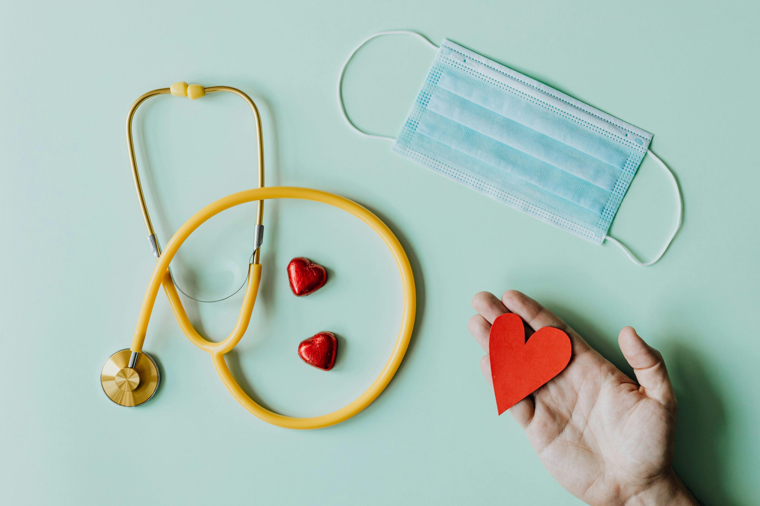 A stethascope, facemask, and person holding a paper heart