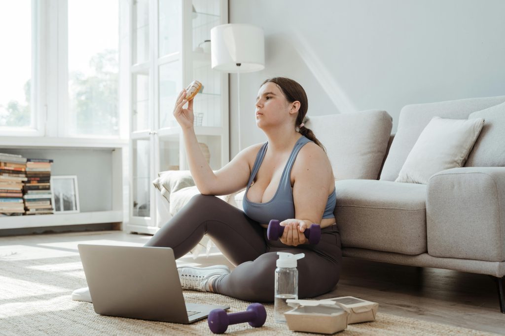 Person sitting on the floor holding a weight in one hand and a doughnut in the other